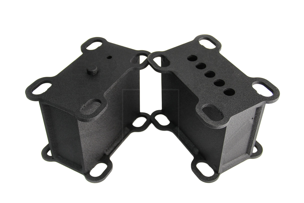 A pair of black metal heavy duty lift blocks for a vehicle, featuring multiple holes for mounting and configuration adjustments.