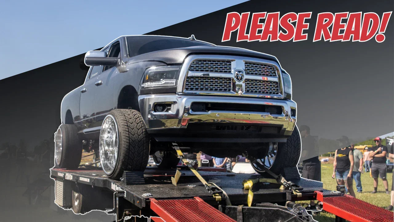 Lifted pickup truck on dyno testing platform at outdoor motorsports event, crowd in background