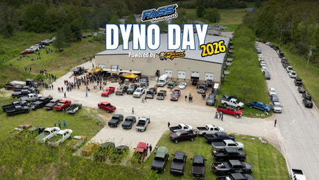 Aerial view of Dyno Day 2026 event with trucks, Jeeps, off-road vehicles and crowd outside a large garage.