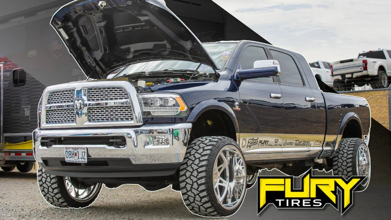 Lifted black truck with aggressive Fury off-road tires, hood open, parked outdoors
