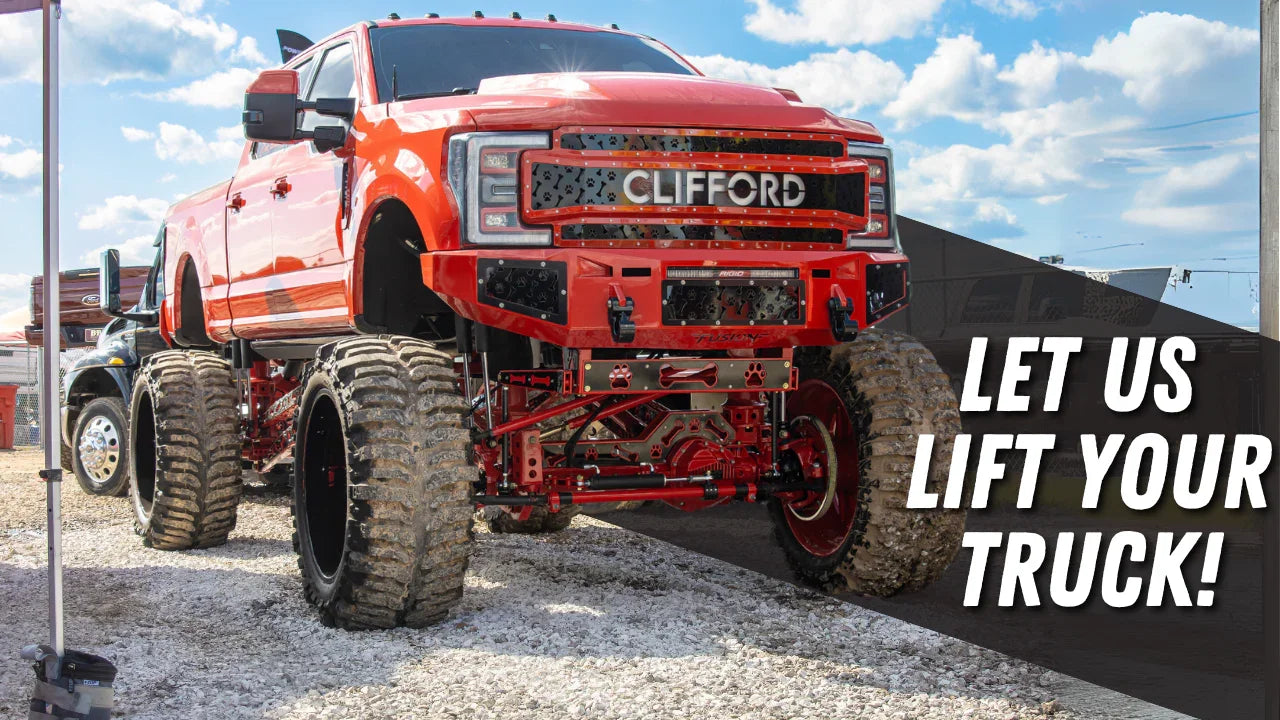 Lifted red truck with large off-road tires and 'Let Us Lift Your Truck' text at outdoor show