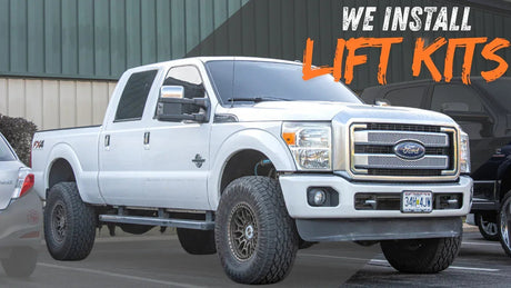 White Ford pickup truck with lift kit installed, parked outside automotive shop