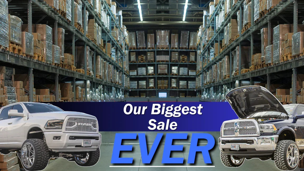 Warehouse with off-road trucks and 'Our Biggest Sale EVER' banner, truck performance parts sale.