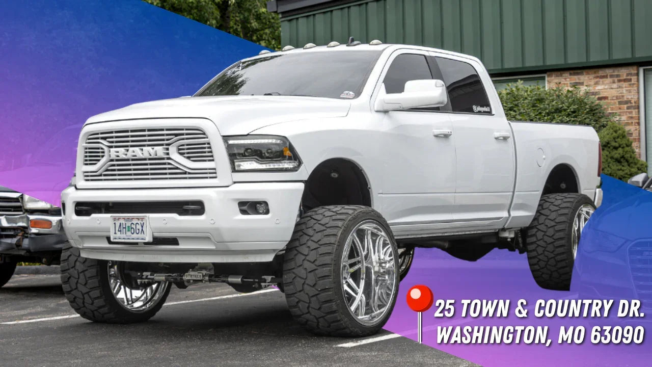 White lifted Ram pickup truck with oversized off-road tires parked outside, Washington MO location address shown.