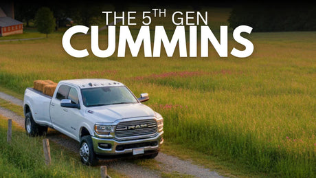 White 5th gen Cummins diesel truck carrying hay on rural dirt road with field background