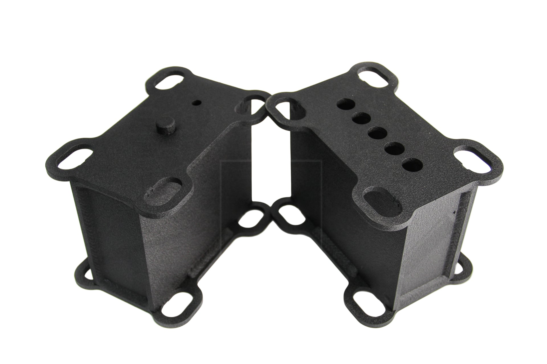 A pair of black metal heavy duty lift blocks for a vehicle, featuring multiple holes for mounting and configuration adjustments.